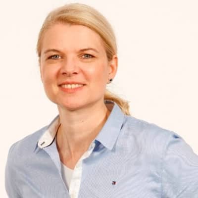  Portrait einer blonden Frau, zum Zopf gebundene Haare. Hellblaue Bluse. Sie lächelt in die Kamera.
