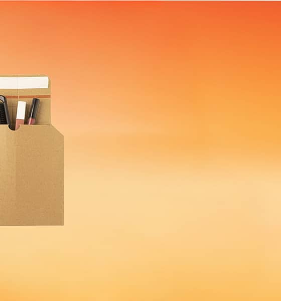 Eine braune Versandtasche ist geöffnet und es schauen ein Kamm und zwei Lipglosse heraus auf orangem Hintergrund.