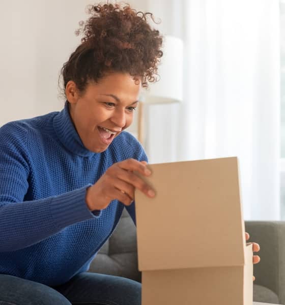 Eine Frau sitzt auf dem Sofa und freut sich, während sie ein Paket öffnet.