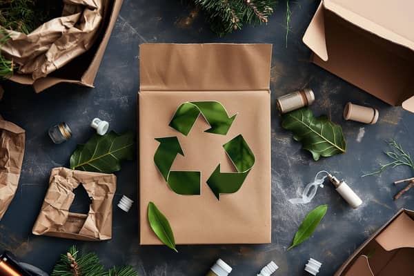 grå baggrund med krøllet papir, grønne blade, grønt genbrugsmærke, grene og plastikpropper m.m.