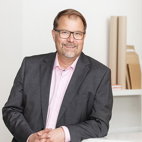 mies katsoo kameraan ja hymyilee, taustalla aaltopahvipakkaukset