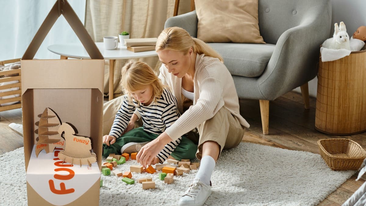 Mutter und Tochter spielen mit Bauklötzen auf dem Boden neben Wellpappverpackung