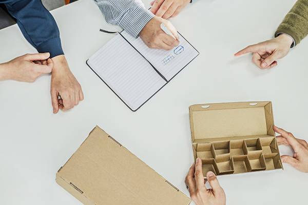 aaltopahvipakkaus keskellä ja käsiä ympärillä