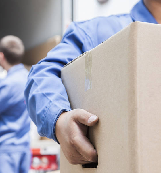 Henkilö kantaa pahvista kuljetuslaatikkoa