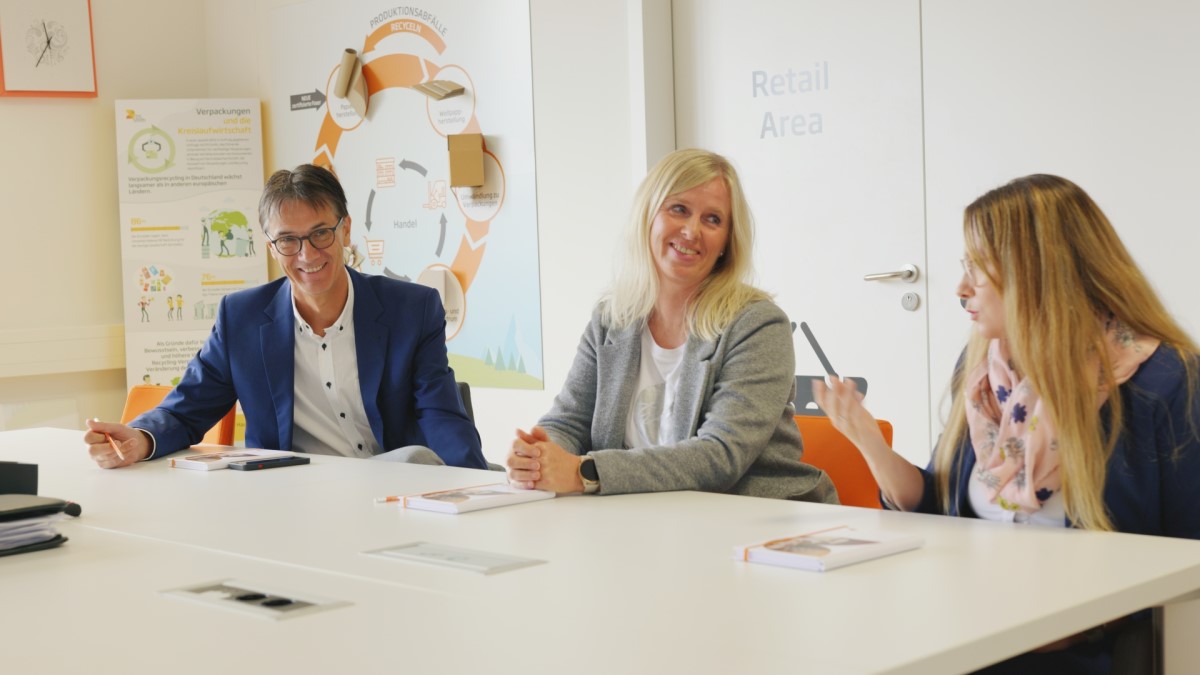 Drei Kolleginnen und Kollegen sitzen gemeinsam am Tisch und unterhalten sich.