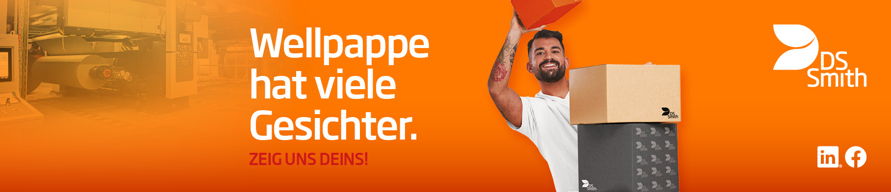 junger dunkelhaariger Mann mit weißem T-Shirt vor orangefarbenen Hintergrund lächelt in die Kamera und schaut an einem Kartonstapel aus Wellpappe vorbei einen hält kleinen Wellpappkarton in der Hand