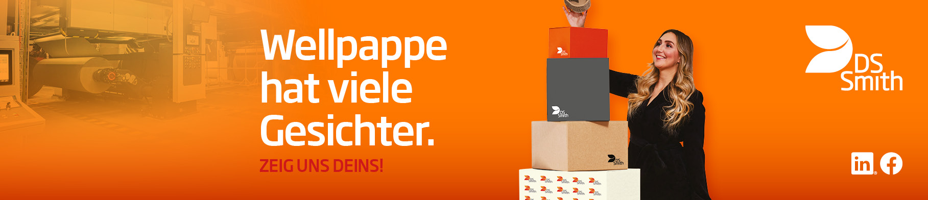  junge blonde Frau in dunklem Kleid steht rechts von einem Wellpappaufsteller und hält einen kleinen Wellpappkarton in der Hand und lächelt.