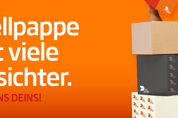 dunkelhaariger junger Mann steht rechts neben und halb hinter einem Kistenstapel aus Wellpappe, freundlich in die Kamera lächelnd, mit einem kleinen Wellpappkarton in der Hand. Mütze und Gehörschutz und oranges T-Shirt, Arbeitskleidung, vor orangefarbenem Hintergrund