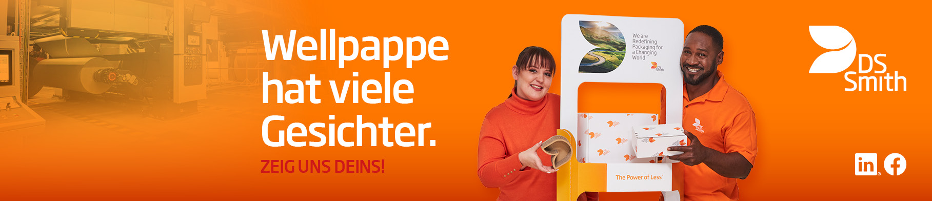 junges Mädchen mit dunklen langen Haaren zum Zopf steht links von einem Aufsteller aus Wellpappe, freundlich in die Kamera lächelnd. Rechts vom Aufsteller steht ein junger farbiger Mann mit schwarzen Haar in organgenem TShirt und lächelt in die Kamera. Beide stehen vor einem orangefarbenen Hintergrund