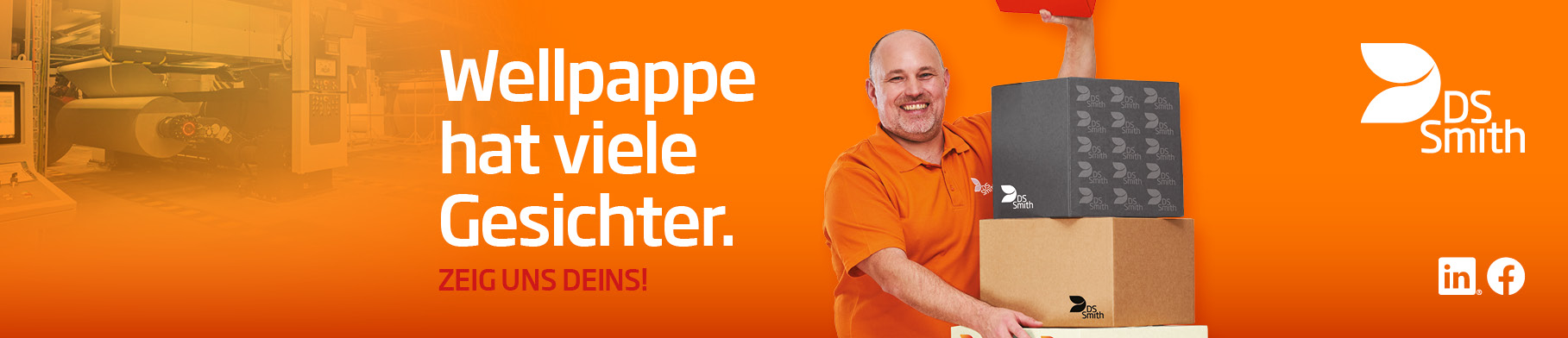 älterer weißer Mann mit kurzem Haar in orangenem T-Shirt steht links neben einem Aufsteller aus Wellpappe, freundlich in die Kamera lächelnd, mit einem kleinen Wellpappkarton in der Hand