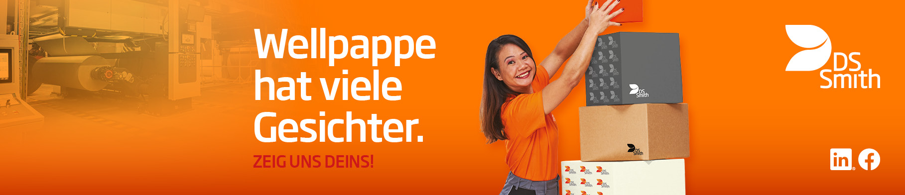 asiatische Frau mit langen Haaren steht seitlich eines Kartonstapels aus Wellpappe vor orangefarbenem Hintergrund und lächelt das Wellpappprodukt in der Hand an. Sie trägt ein orangefarbenes T-Shirt was deutlich Arbeitskleidung der Produktion ist.