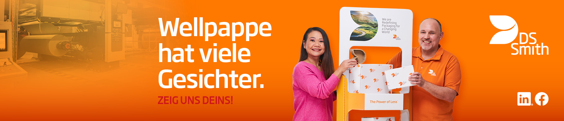  Links vom Aufsteller aus Wellpappe steht eine asiatische Frau mit langem schwarzen Haar in pinkfarbenen T-Shirt und lächelt in die Kamera. Rechts steht älterer weißer Mann mit kurzem Haar in orangenem T-Shirt steht links neben einem Kistenstapel aus Wellpappe, freundlich in die Kamera lächelnd, mit einem kleinen Wellpappkarton in der Hand