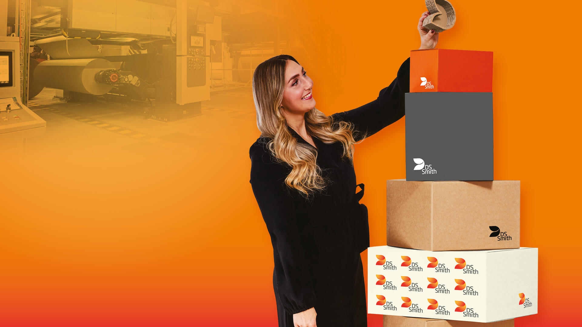 junge blonde Frau in dunklem Kleid steht links von einem Wellpappaufsteller und hält einen kleinen Wellpappkarton in der Hand und lächelt.