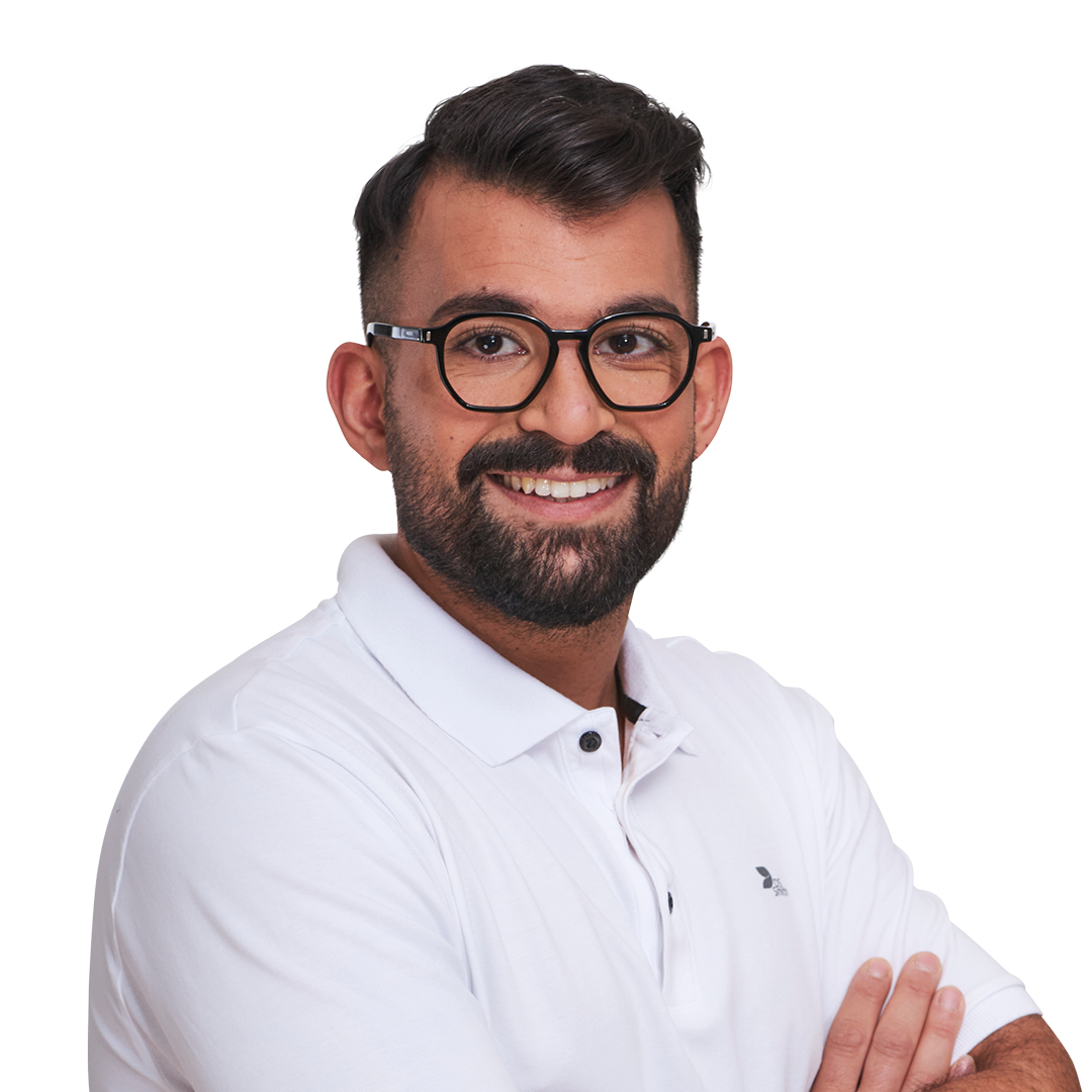 Portrait eines jungen Mannes, Bart, schwarze Brille, weißes T-Shirt. Vor der Brust verschränkte Arme. Es handelt sich um legere Bekleidung für das Büro (Design). Er lächelt in die Kamera.