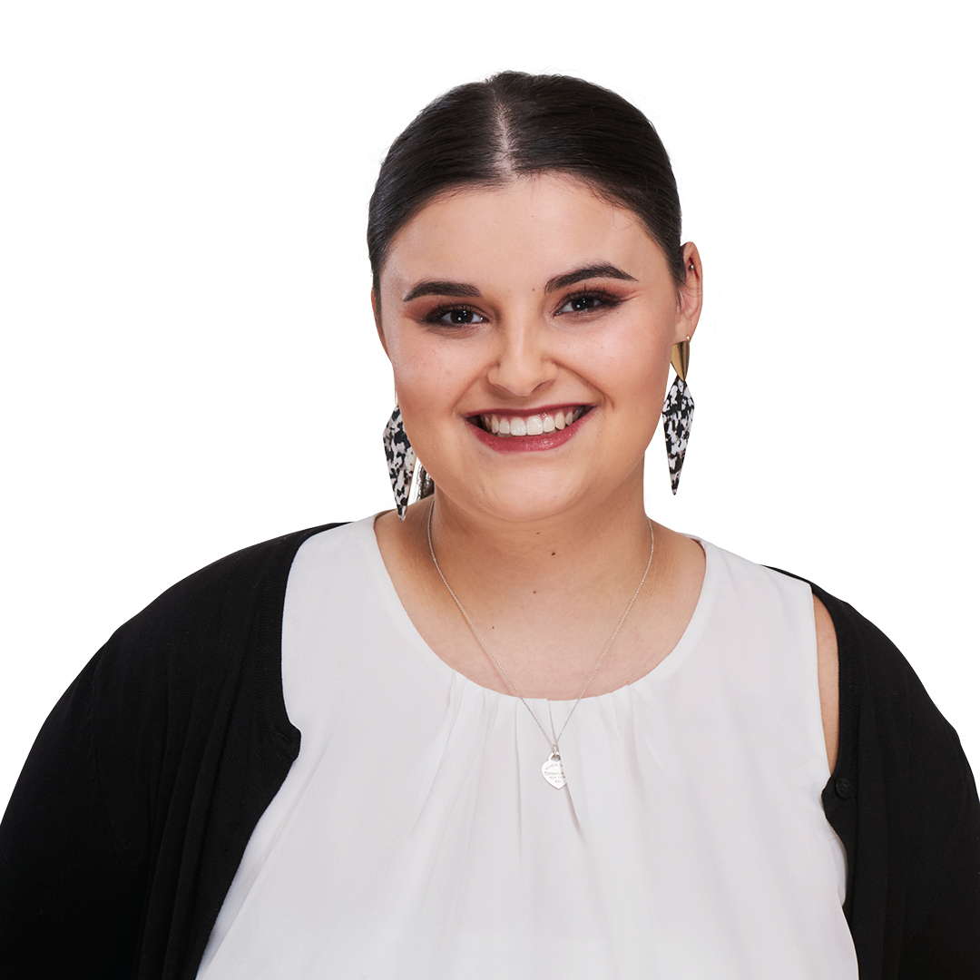 Portrait einer jungen dunkelhaarigen Frau mit Zopf in weißer Bluse mit dunkler Strickjacke im Büro Look. Sie lächelt in die Kamera.