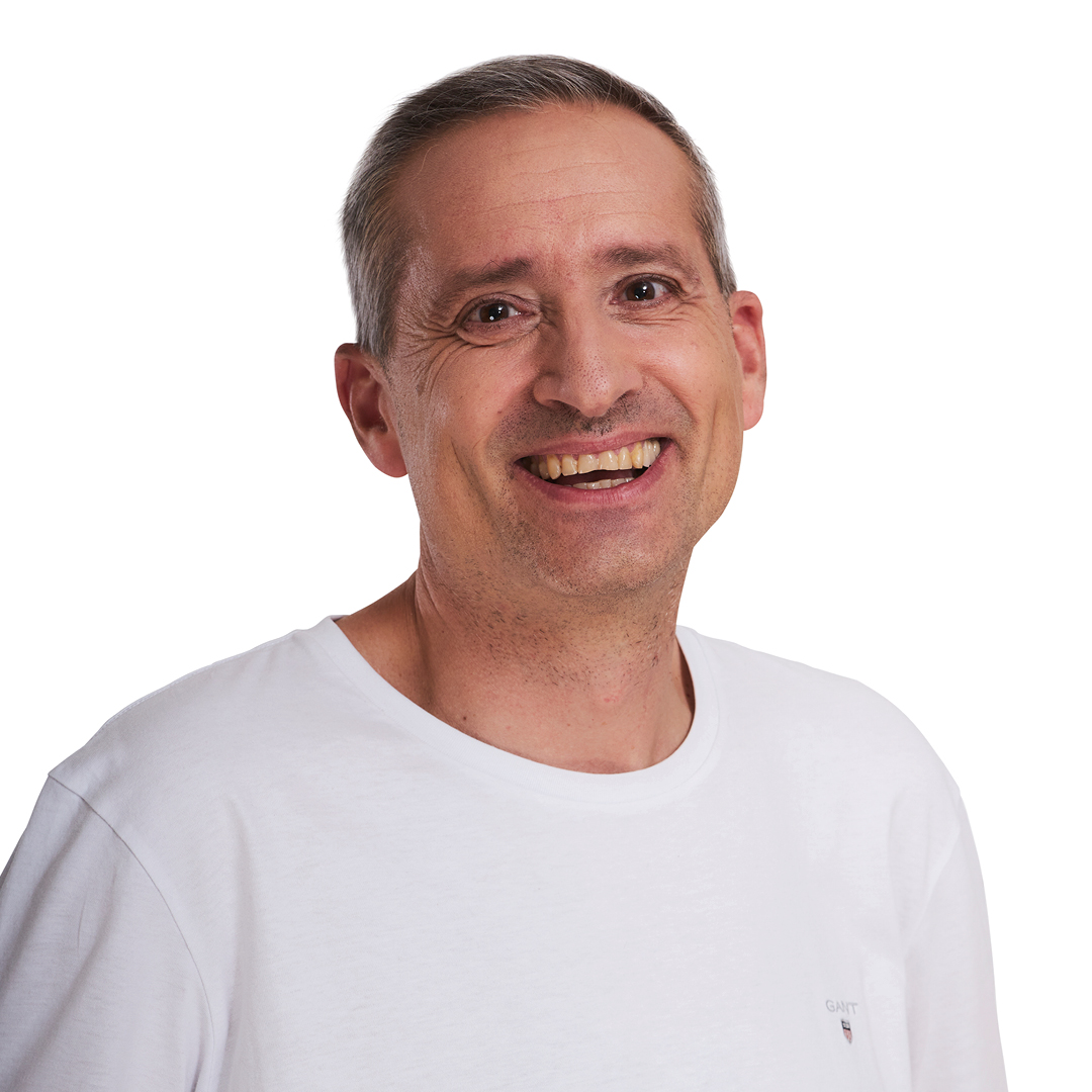 Portrait eines älteren weißen Mannes mit kurzem Haar in weißem T-Shirt. Er lächelt mit geneigtem Kopf in die Kamera.