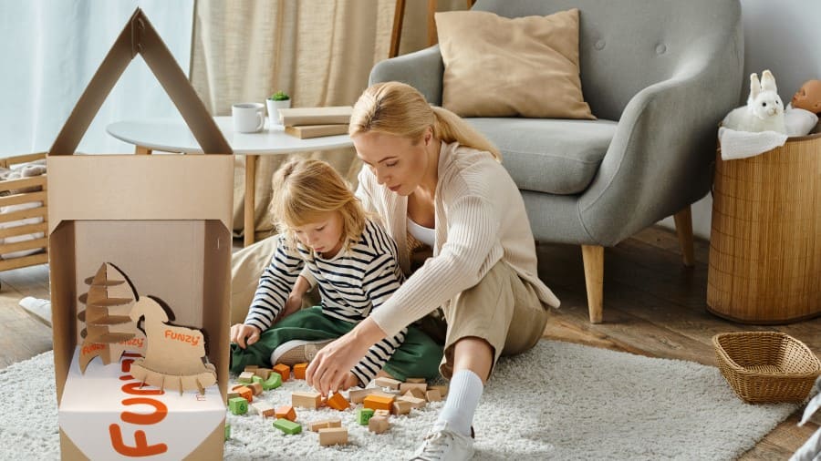 Mutter und Tochter spielen mit Bauklötzen auf dem Boden nebenWellpappverpackung