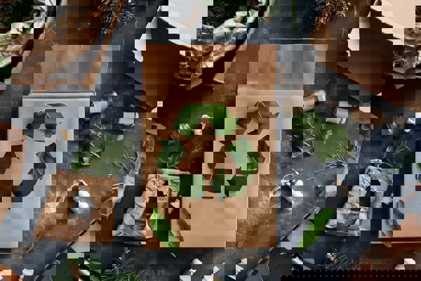 grå baggrund med krøllet papir, grønne blade, grønt genbrugsmærke, grene og plastikpropper m.m.