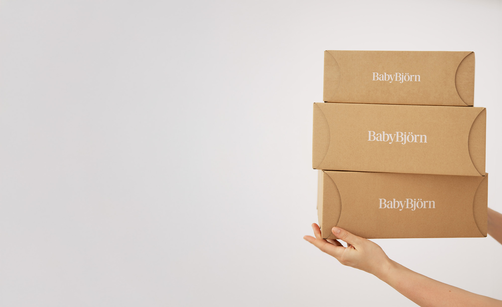 En hand håller upp tre staplade, bruna kartonger märkta "BabyBjörn".