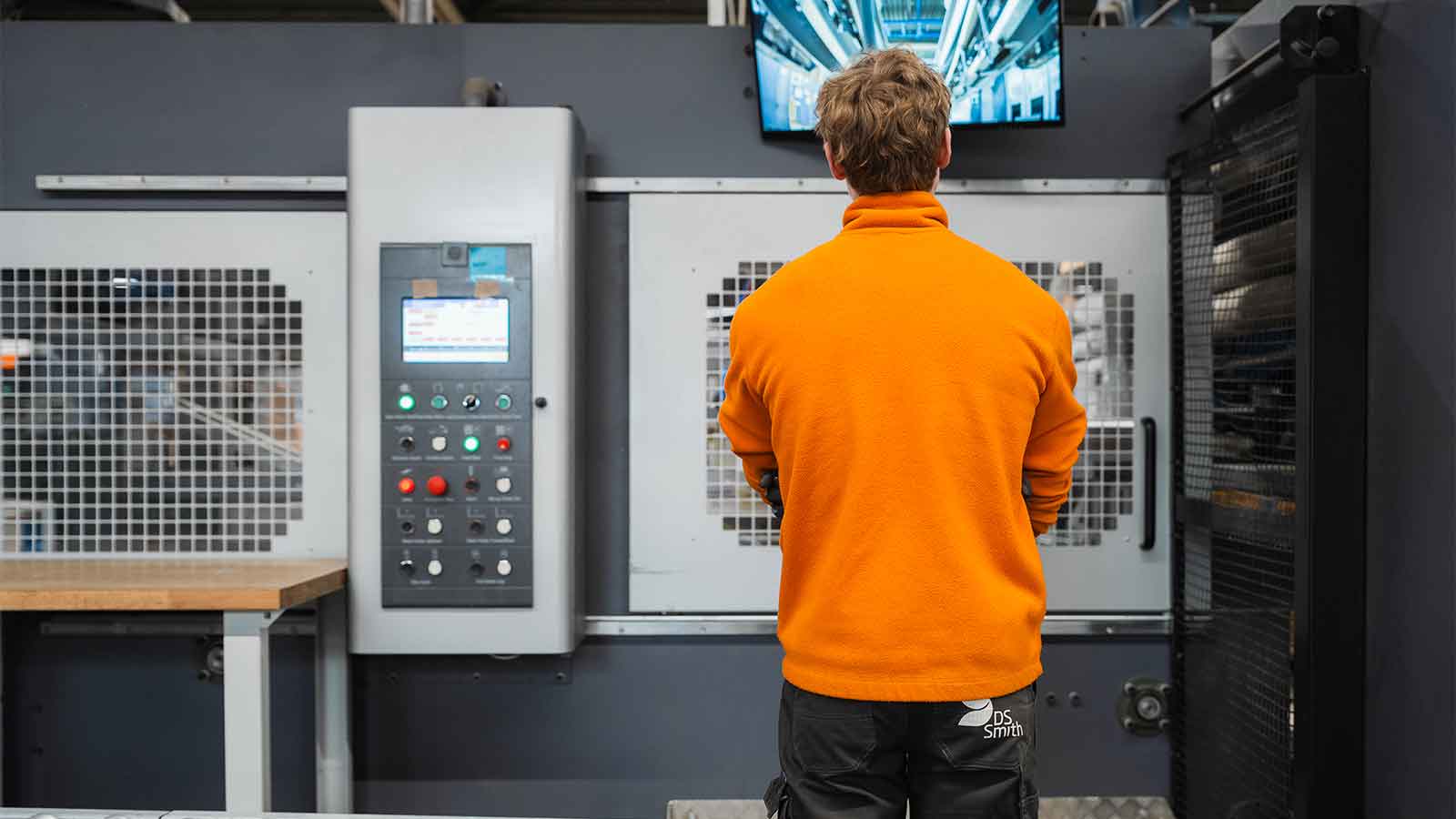 Man in oranje vest bestudeert een machine als operator bij DS Smith.